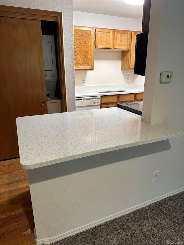 kitchen with stacked washer / dryer, light stone countertops, white dishwasher, and kitchen peninsula