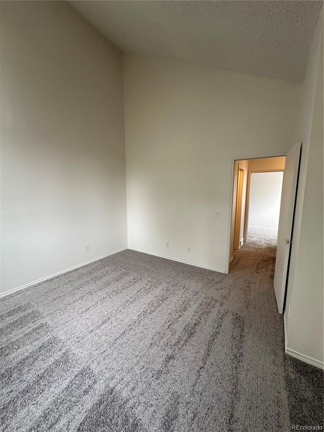 spare room featuring dark colored carpet, vaulted ceiling, and a textured ceiling