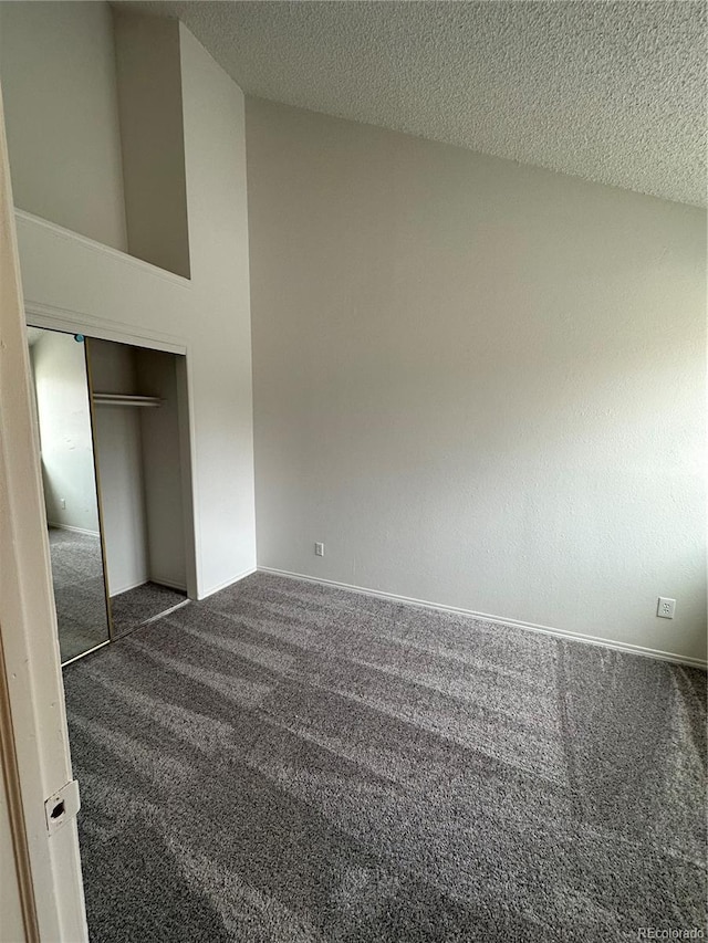 spare room with high vaulted ceiling, a textured ceiling, and dark colored carpet