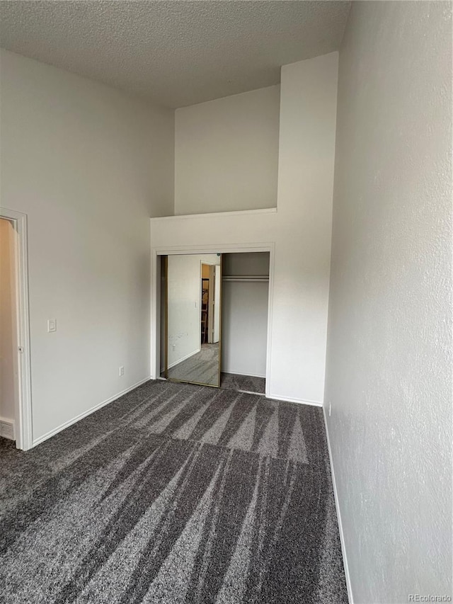 unfurnished bedroom featuring a high ceiling, a closet, a textured ceiling, and dark colored carpet