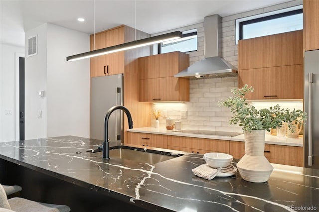 kitchen featuring backsplash, sink, wall chimney exhaust hood, stainless steel refrigerator, and electric stovetop