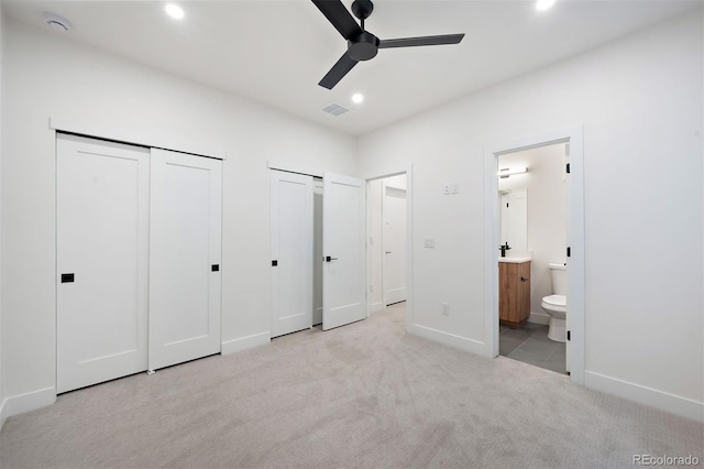 unfurnished bedroom featuring light carpet, two closets, sink, ensuite bath, and ceiling fan