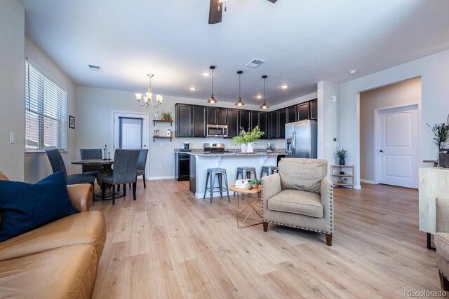 living area with light wood-type flooring, ceiling fan with notable chandelier, baseboards, and visible vents