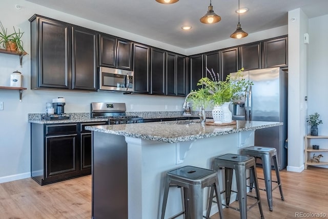 kitchen featuring stainless steel appliances, a sink, open shelves, a breakfast bar, and light stone countertops