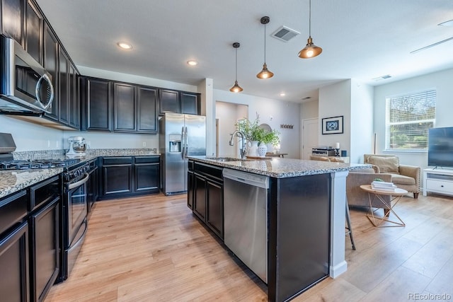 kitchen featuring stainless steel appliances, light wood-style flooring, a sink, visible vents, and light stone counters