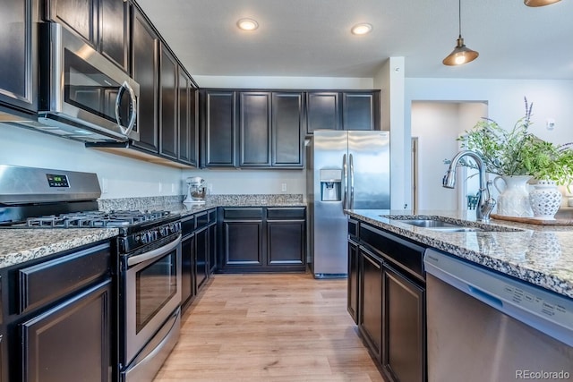 kitchen with light stone countertops, light wood finished floors, stainless steel appliances, and a sink