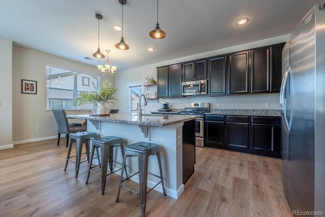 kitchen featuring a sink, a chandelier, stainless steel appliances, a kitchen bar, and light stone countertops