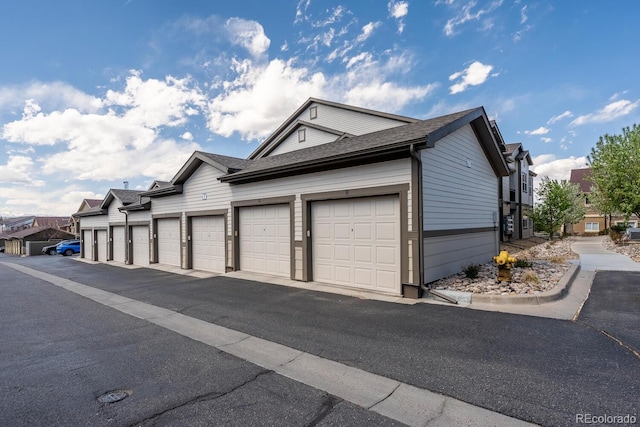 view of side of property with a residential view, community garages, and a shingled roof