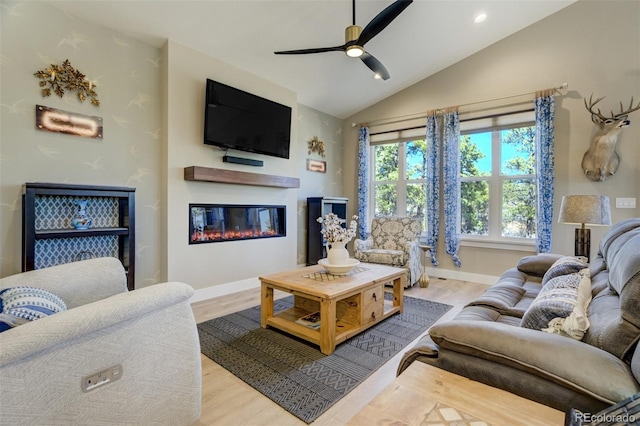 living room featuring ceiling fan, baseboards, vaulted ceiling, wood finished floors, and a glass covered fireplace