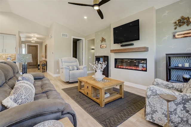 living room with visible vents, light wood-style floors, lofted ceiling, and a glass covered fireplace