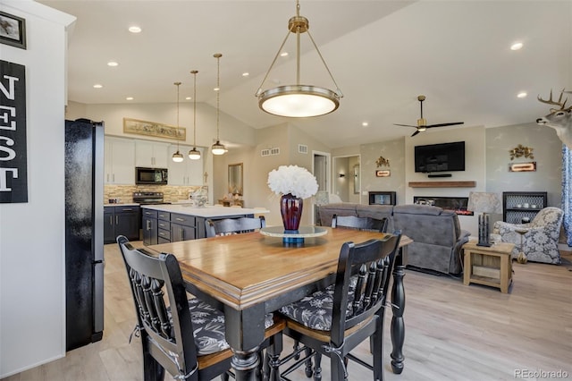 dining area with a glass covered fireplace, vaulted ceiling, light wood-style floors, and ceiling fan