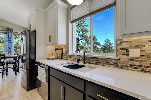 kitchen featuring dishwasher, light countertops, decorative backsplash, freestanding refrigerator, and a sink