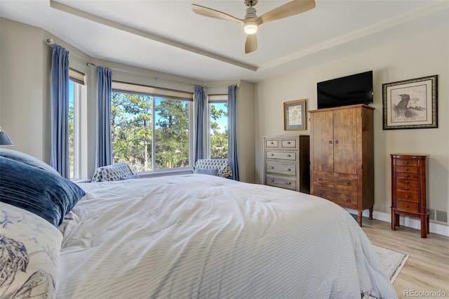 bedroom featuring a raised ceiling, light wood-style floors, baseboards, and ceiling fan