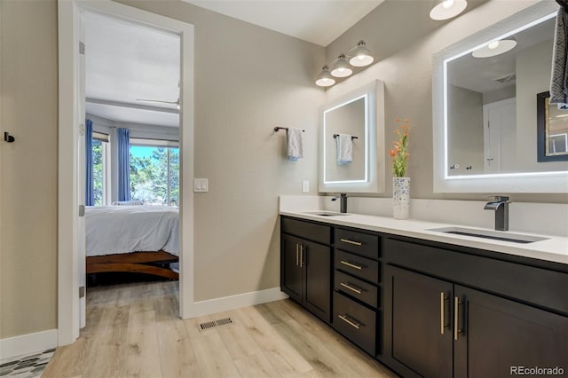 ensuite bathroom with a sink, visible vents, wood finished floors, and double vanity