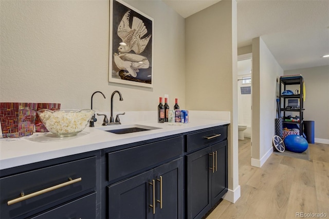 bar with a sink, light wood-type flooring, baseboards, and wet bar