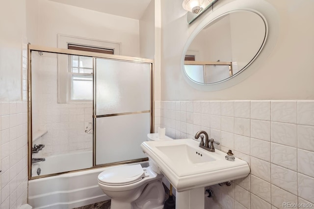 bathroom featuring bath / shower combo with glass door, toilet, and tile walls