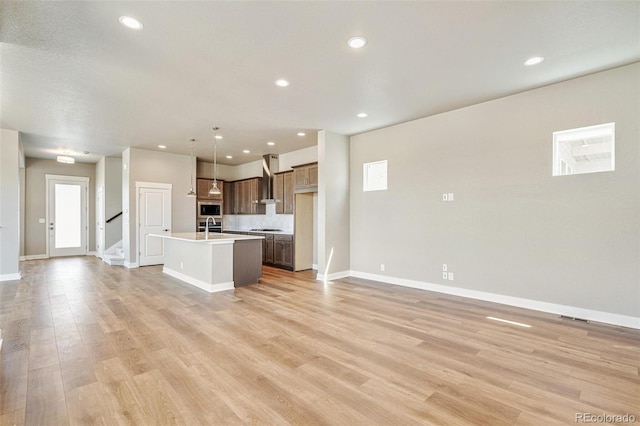 21022 E 63rd Dr, Aurora, CO 80019 - kitchen with pendant lighting, an island with sink, sink, light hardwood / wood-style flooring, and wall chimney exhaust hood