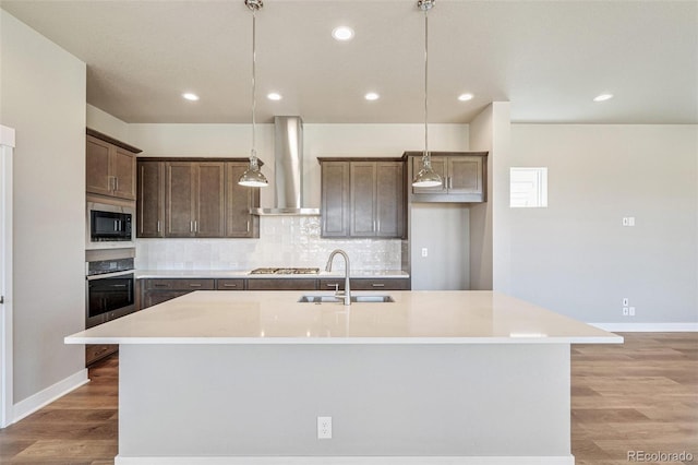 21022 E 63rd Dr, Aurora, CO 80019 - kitchen featuring pendant lighting, wall chimney range hood, sink, tasteful backsplash, and an island with sink