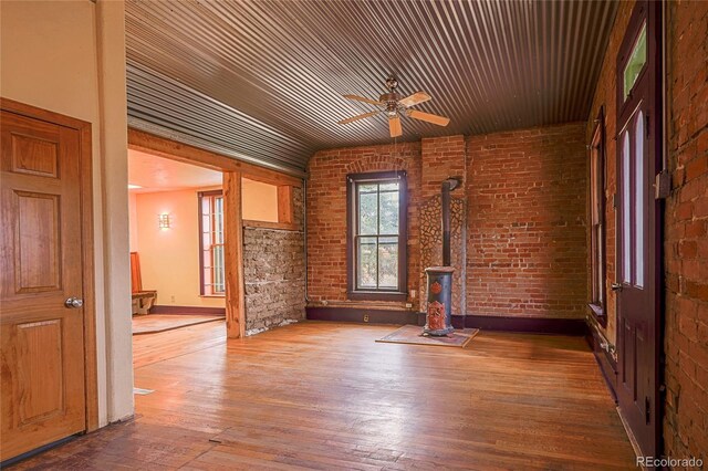 unfurnished room with a wood stove, ceiling fan, wood ceiling, hardwood / wood-style flooring, and brick wall