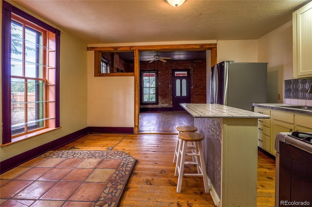 kitchen featuring a breakfast bar area, tile countertops, stainless steel appliances, ceiling fan, and light wood-type flooring