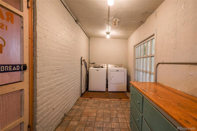 laundry area with brick wall, a textured ceiling, cabinets, and washer and clothes dryer