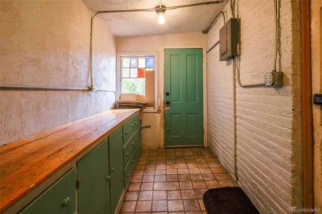 interior space with a textured ceiling, butcher block countertops, green cabinets, electric panel, and lofted ceiling