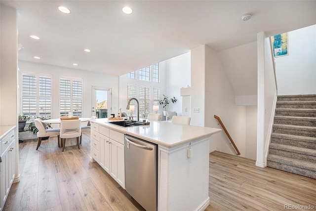 kitchen with an island with sink, white cabinets, stainless steel dishwasher, light hardwood / wood-style flooring, and sink