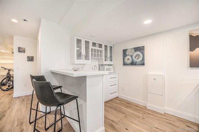 kitchen with white cabinets, sink, kitchen peninsula, a breakfast bar, and light hardwood / wood-style flooring