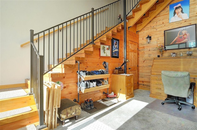 staircase featuring carpet flooring, wood walls, and high vaulted ceiling