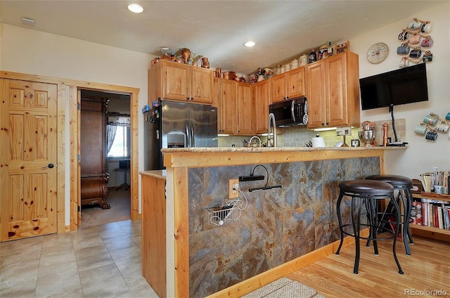 kitchen with a breakfast bar area, stainless steel fridge, backsplash, kitchen peninsula, and light wood-type flooring