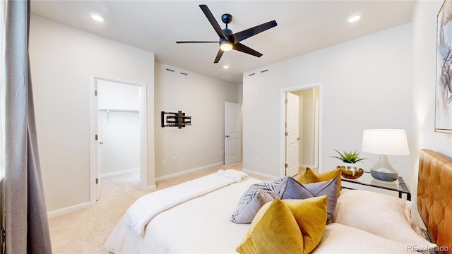 bedroom with ceiling fan, a walk in closet, light carpet, and a closet