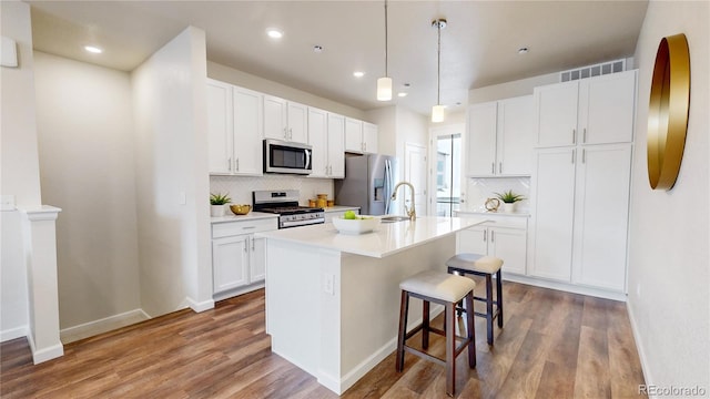 kitchen with white cabinets, appliances with stainless steel finishes, a kitchen island with sink, and hardwood / wood-style floors