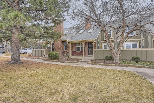 view of front facade featuring a shingled roof, a chimney, fence, a front lawn, and brick siding