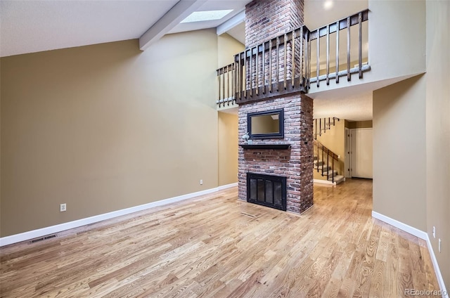 unfurnished living room featuring a fireplace, wood finished floors, visible vents, baseboards, and beam ceiling