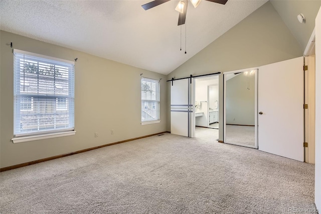 unfurnished bedroom featuring high vaulted ceiling, light carpet, baseboards, and a barn door