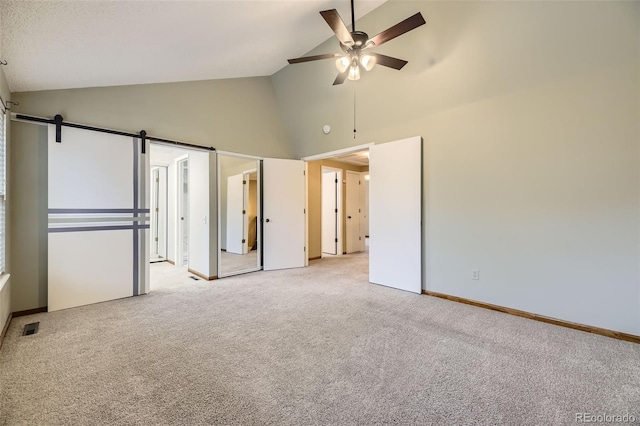 unfurnished bedroom with carpet floors, visible vents, a barn door, high vaulted ceiling, and baseboards