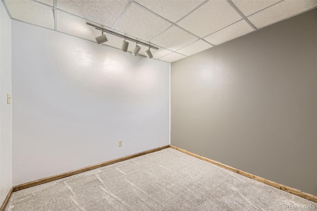 carpeted empty room featuring rail lighting, a drop ceiling, and baseboards