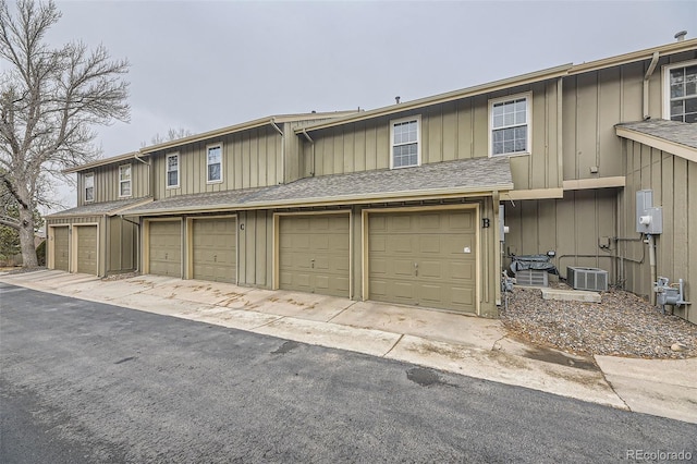 townhome / multi-family property featuring board and batten siding, central AC, roof with shingles, and community garages