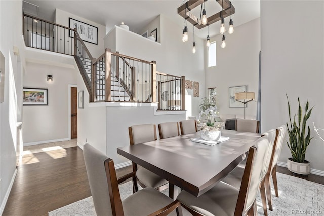 dining area featuring a towering ceiling, stairs, baseboards, and wood finished floors