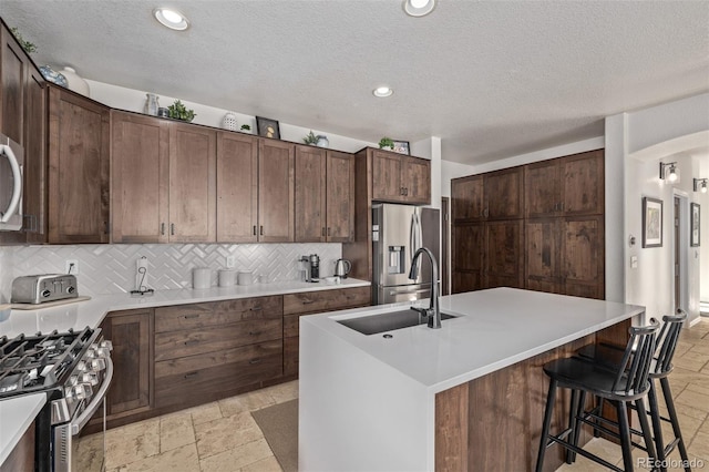 kitchen with stone tile floors, appliances with stainless steel finishes, a sink, light countertops, and backsplash