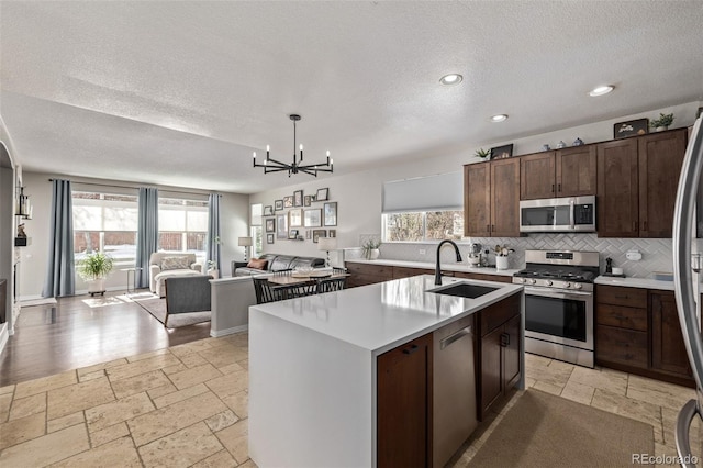 kitchen featuring stone tile floors, stainless steel appliances, a sink, open floor plan, and light countertops