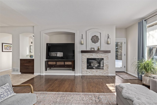 living room featuring baseboards, visible vents, wood finished floors, and a stone fireplace