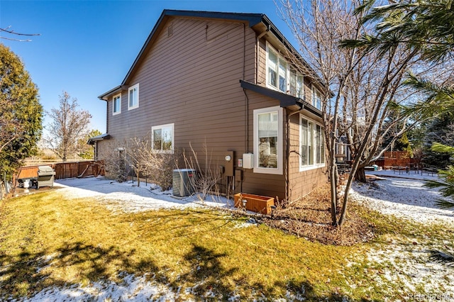 view of snow covered exterior with a yard, central AC unit, and fence