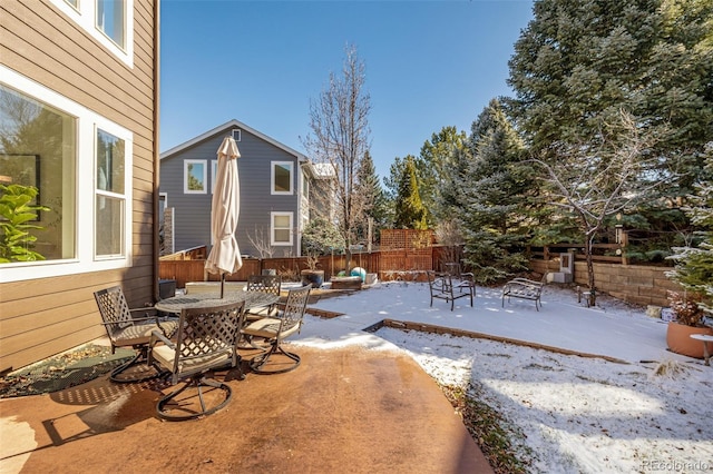 snow covered patio featuring outdoor dining area and fence