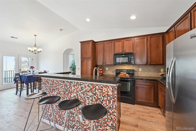 kitchen with arched walkways, a chandelier, a kitchen bar, black appliances, and lofted ceiling