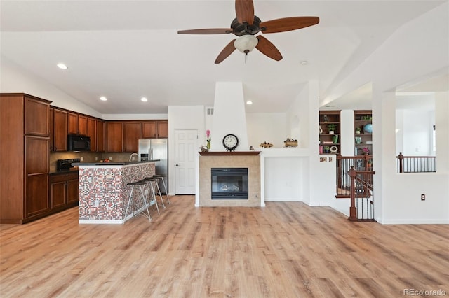 kitchen with stainless steel refrigerator with ice dispenser, open floor plan, light wood-style floors, black microwave, and vaulted ceiling