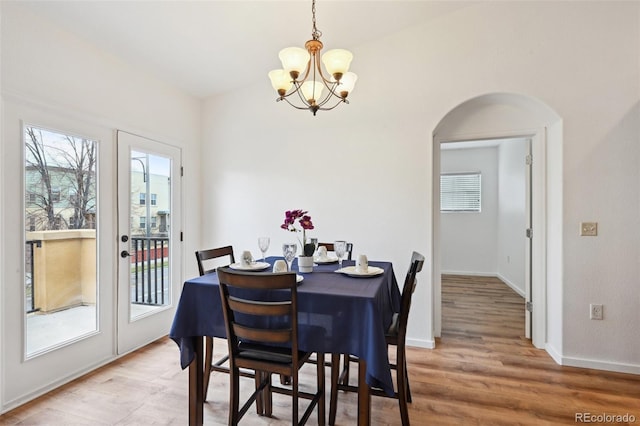 dining area featuring a chandelier, arched walkways, a healthy amount of sunlight, and light wood finished floors