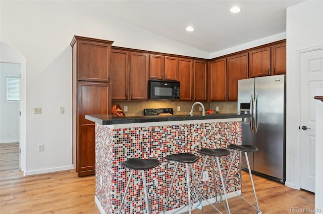 kitchen featuring light wood-type flooring, a kitchen breakfast bar, black appliances, and decorative backsplash