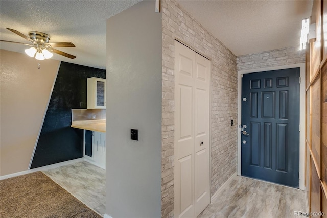 entryway with a textured ceiling, ceiling fan, wood finished floors, and brick wall