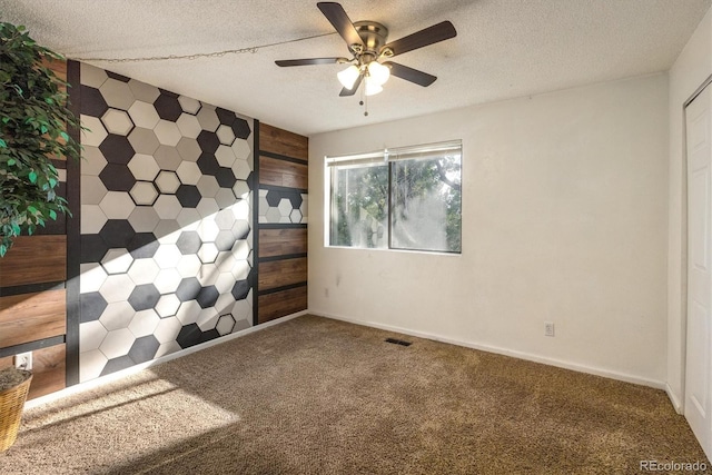 carpeted spare room with a textured ceiling, visible vents, and a ceiling fan
